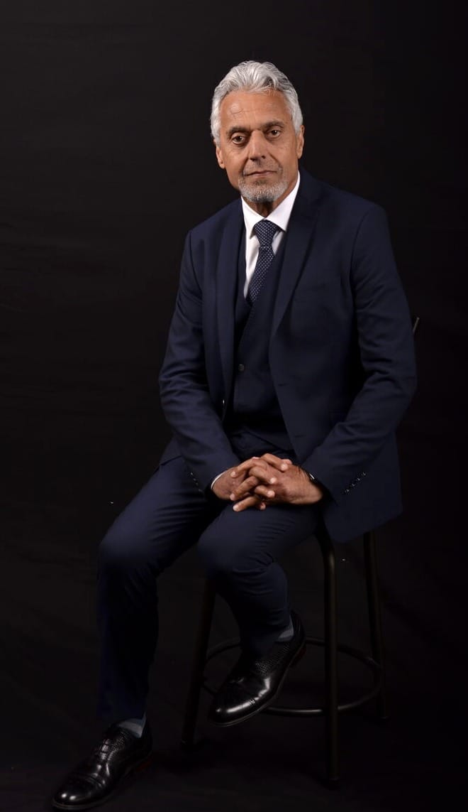 Atta Arghandiwal in a dark suit, lit from one side against a deep background, looking directly at the viewer.